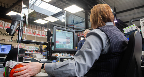 An einer Supermarkt-Kasse wird die Kassiererin mit einer Plexiglasscheibe geschützt.(Bild: © picture alliance/Tom Weller/dpa)