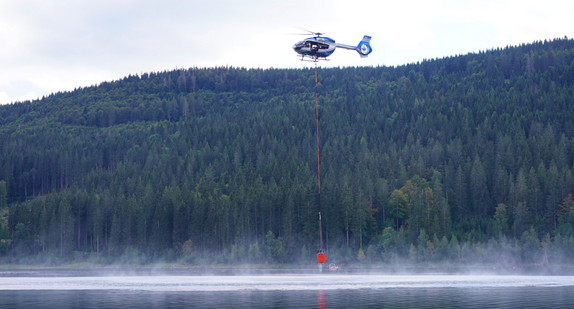 Polizeihubschrauber mit Außenlöschbehälter nimmt Wasser aus dem Schluchsee auf.