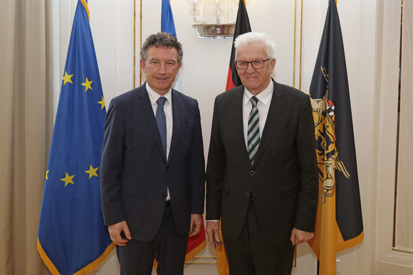 Ministerpräsident Winfried Kretschmann (rechts) und Franck Leroy (links), Präsident der Région Grand Est, stehen in der Villa Reitzenstein vor Fahnen.