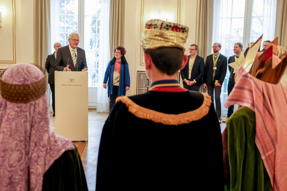 Ministerpräsident Winfried Kretschmann (hinten links) spricht zu den Sternsingerinnen und Sternsingern.