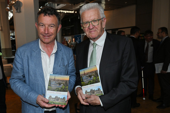 Ministerpräsident Winfried Kretschmann (rechts)  und der Präsident der Région Grand Est, Franck Leroy (links), jeweils mit einem Buch in der Hand.