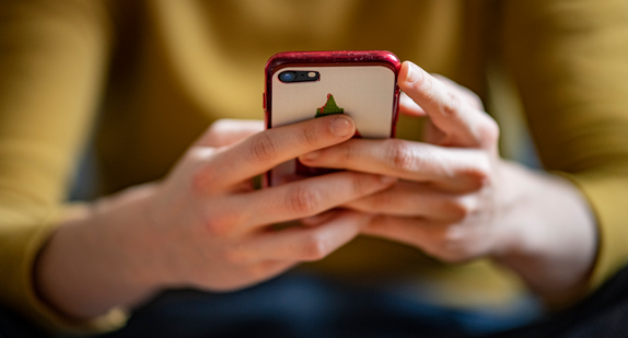 Eine junge Frau mit gelbem Pullover hält ein Smartphone in der Hand.