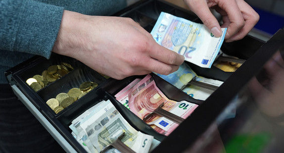 Hände eines Kioksmitarbeiters legen Geld in eine Kasse.