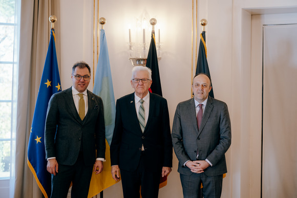 Von links nach rechts: Der ukrainische Botschafter Oleksij Makeiev, Ministerpräsident Winfried Kretschmann und der ukrainische Generalkonsul Yurii Nykytiuk stehen vor Fahnen.