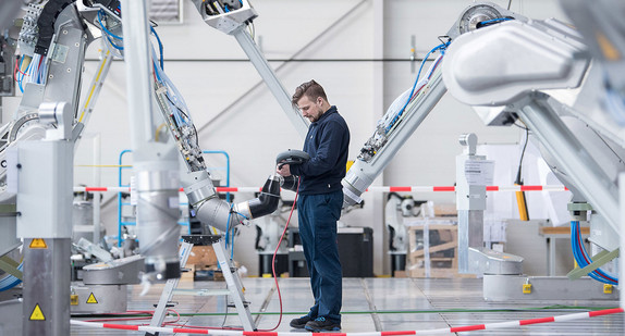 Ein Mitarbeiter testet einen Lackierroboter (Bild: © dpa).