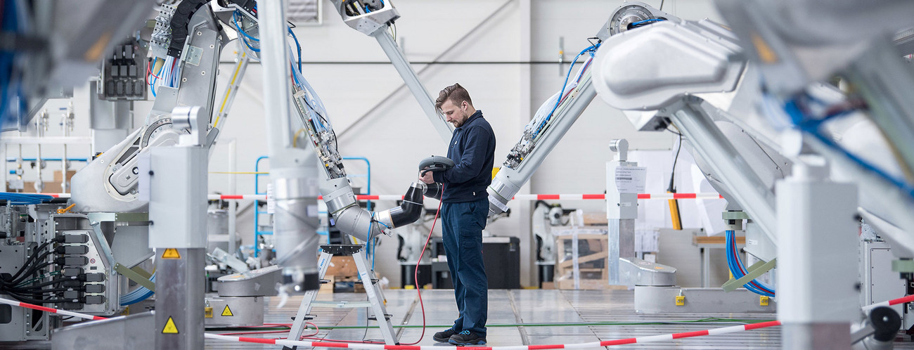 Ein Mitarbeiter testet einen Lackierroboter (Bild: © dpa).