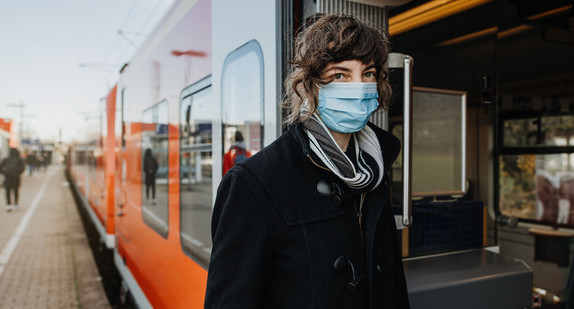 Eine Frau mit einer medizinischen Maske steigt in einen Nahverkehrszug ein.