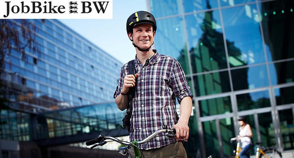 Radfahrer in legerer Arbeitskleidung steht mit Rad und Helm vor einem Bürogebäude