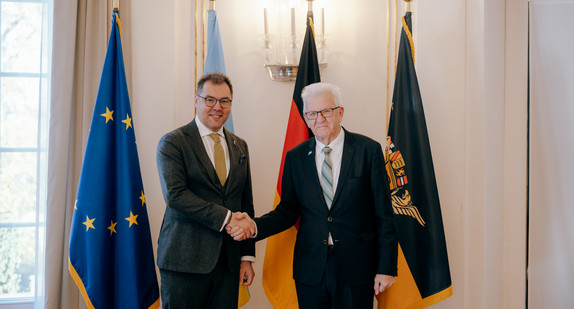 Ministerpräsident Winfried Kretschmann (rechts) und der ukrainische Botschafter Oleksij Makeiev (links) stehen vor Fahnen und geben sich die Hand.