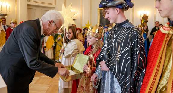 Ministerpräsident Winfried Kretschmann (links) überreicht den Sternsingerinnen und Sternsingern eine Geldspende.