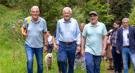 Landrat Riegger, Ministerpräsident Kretschmann und Verkehrsminister Hermann laufen vor einer Wandergruppe und schauen in die Kamera.