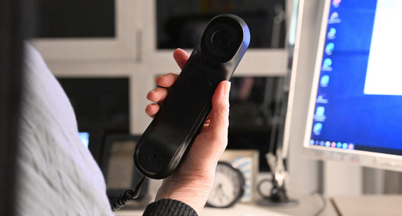 Eine Person nimmt einen Telefonhörer ab.