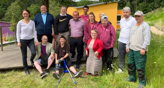 Philipp Einhäuser und Simone Fischer posieren auf dem Gelände der Laufenmühle mit weiteren Mitarbeitenden und dem Bewohnerbeirat und Werkstattrat der Laufenmühle für ein Gruppenfoto.