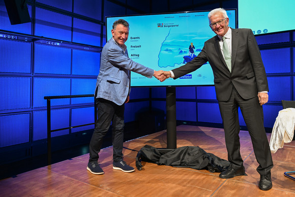 Ministerpräsident Winfried Kretschmann (rechts) und der Präsident der Région Grand Est, Franck Leroy (links), geben sich vor einer Videowand mit dem neuen Bürgerportal die Hand.