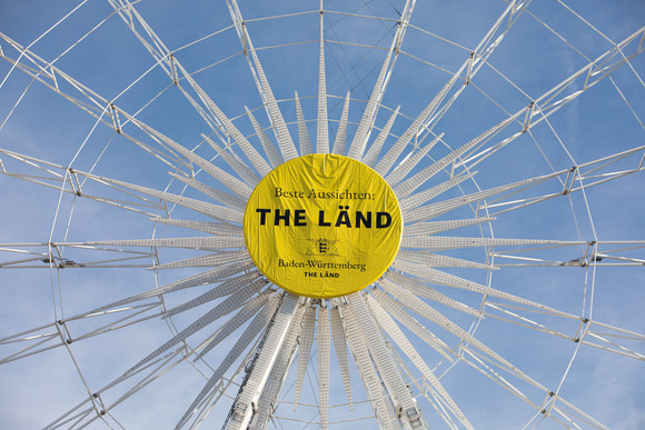 Riesenrad auf dem Stuttgarter Schlossplatz mit der Aufschrift „Beste Aussichten: THE LÄND“ und dem Landeswappen