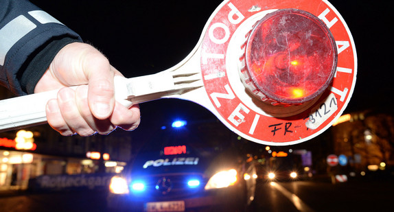 Eine Haltekelle der Polizei ist bei einer Kontrolle vor einem Polizeifahrzeug zu sehen. (Foto: © dpa)