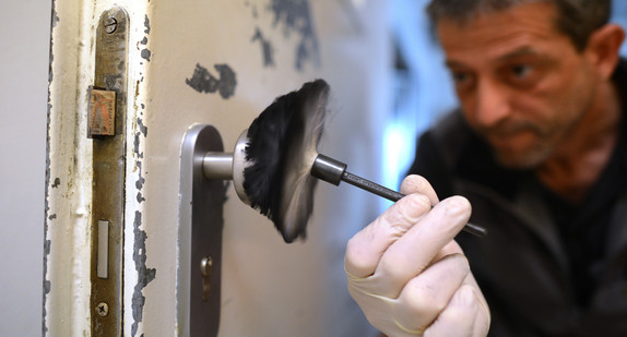 Ein kriminaltechnischer Angestellter der Polizei sichert Spuren an einer Eingangstür. (Foto: © dpa)