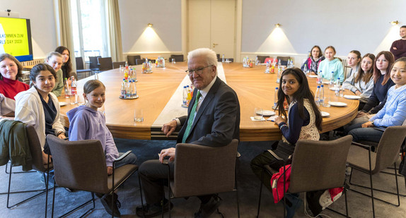 Ministerpräsident Winfried Kretschmann (Mitte) sitzt mit 12 Schülerinnen am Kabinettstisch im Kabinettssaal in der Villa Reitzenstein.