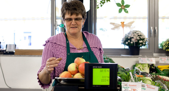 Eine Obstverkäuferin wiegt in einem Bauernladen Äpfel.