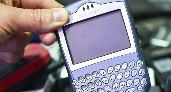 Eine Hand hält in einer Recyclingfirma ein ausgedientes Mobiltelefon. (Foto: dpa)