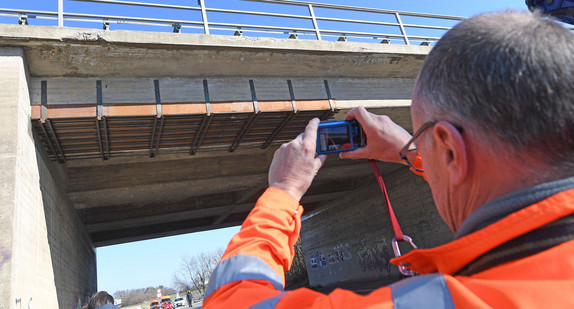 Straßenwärter fotografiert einen Schaden an einer Brücke.