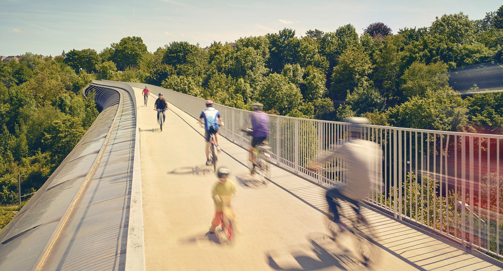 Unscharf verwischte Radfahrer fahren auf einer Radbrücke über ein Tal.