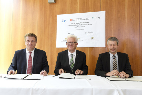 Ministerpräsident Winfried Kretschmann (M.) sowie die Parlamentarischen Staatssekretäre Thomas Bareiß (l., Bundesministerium für Wirtschaft und Energie) und Steffen Bilger (r., Bundesministerium für Verkehr und digitale Infrastruktur) unterzeichnen eine Absichtserklärung zum Projekt HyFab, einer Forschungsfabrik für Brennstoffzellen und Wasserstoff (Bild: © e-mobil BW / Studio KD Busch)