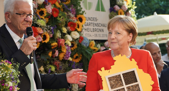 Ministerpräsident Winfried Kretschmann (l.) überreicht Bundeskanzlerin Angela Merkel (r.) bei der 55. Stallwächterparty der baden-württembergischen Landesvertretung in Berlin ein Bienenhotel mit den Umrissen des Landes Baden-Württemberg als Geschenk. (Foto: © dpa)