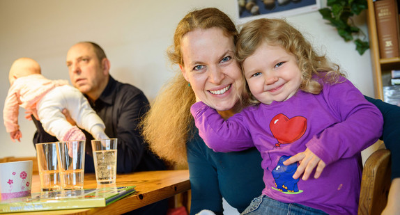 Eltern sitzen mit ihren beiden Kindern im Wohnzimmer (Bild: © dpa).