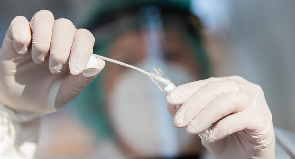 Ein Mitarbeiter zeigt in einer Corona-Abstrichstelle einen Abstrich für einen Corona-Test.