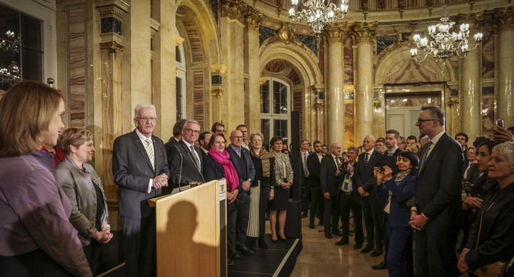 Ministerpräsident Winfried Kretschmann (Dritter von links) spricht zu den Gästen, neben ihm stehen die Mitglieder der Landesregierung.