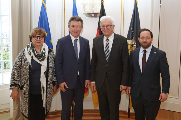 von links nach rechts: Brigitte Torloting, Vizepräsidentin der Région Grand Est, Franck Leroy, Präsident der Région Grand Est, Ministerpräsident Winfried Kretschmann und Staatssekretär Florian Hassler stehen in der Villa Reitzenstein vor Fahnen.