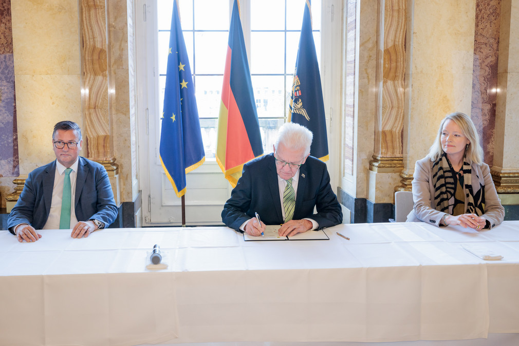 Ministerpräsident Winfried Kretschmann (Mitte) unterzeichnet den Gesellschaftsvertrag für die Zukunft der Landwirtschaft und der biologischen Vielfalt in Baden-Württemberg, daneben sitzen Landwirtschaftsminister Peter Hauk (links) und Umweltministerin Thekla Walker (rechts).