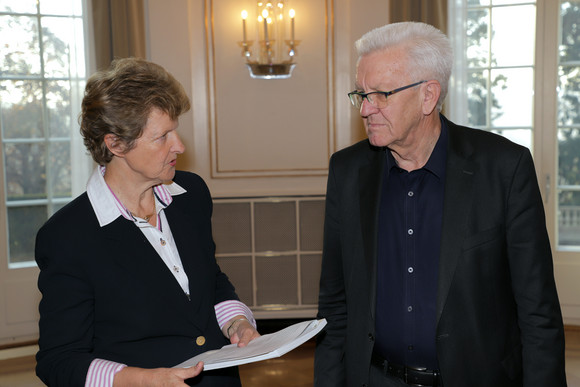 Die Vorsitzende des Normenkontrollrats Baden-Württemberg, Dr. Gisela Meister-Scheufelen (l.), übergibt Ministerpräsident Winfried Kretschmann (r.) eine Studie zur Bürokratieentlastung im Ehrenamt. (Bild: Staatsministerium Baden-Württemberg