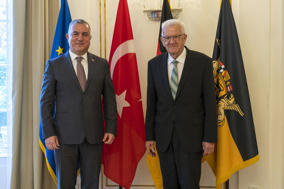 Ministerpräsident Winfried Kretschmann (rechts) und der türkische Botschafter Ahmet Başar Şen (links) stehen in der Villa Reitzenstein vor Fahnen.