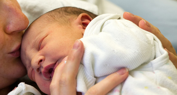 Eine Mutter küsst ihr Baby auf den Kopf (Bild: © dpa).