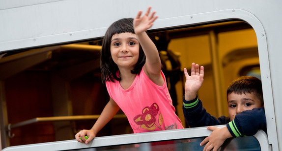 Ein kleiner Junge und ein Mädchen winken auf dem Hauptbahnhof in München bei der Abfahrt eines Sonderzuges, der die Flüchtlinge auf andere Bundesländer verteilt (Bild: © dpa).