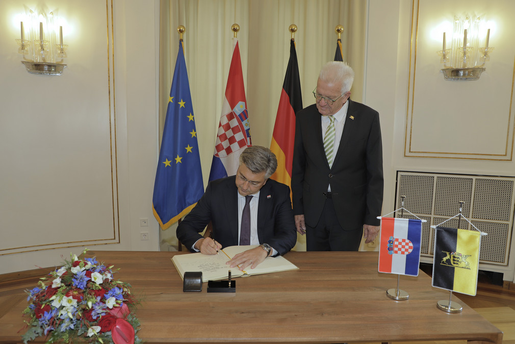 Ministerpräsident Winfried Kretschmann (rechts, stehend) und der kroatische Premierminister Andrej Plenković (links, sitzend) beim Eintrag in das Gästebuch der Landesregierung