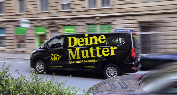 Ein fahrendes schwarzes Auto mit gelber Aufschrift "Deine Mutter fährt nicht betrunken" und Team Vision Zero.