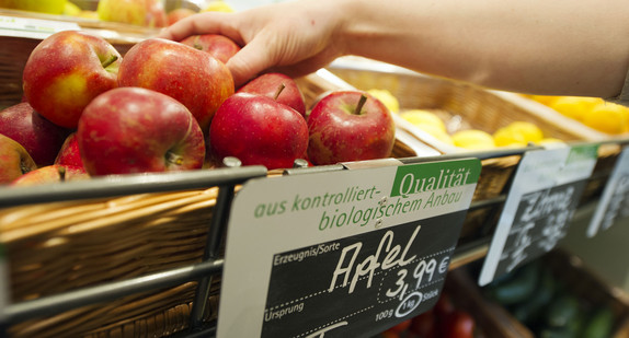 Eine Frau greift nach einem Apfel aus dem Obst- und Gemüseregal eines Reformhauses. (Foto: © dpa)