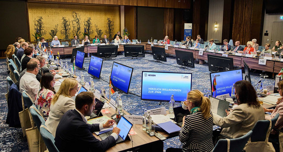 Teilnehmende der Jugend- und Familienministerkonferenz 2026 sitzen mit Blick auf mehrere kreisförmig angeordnete Bildschirme an einem großen Konferenztisch.