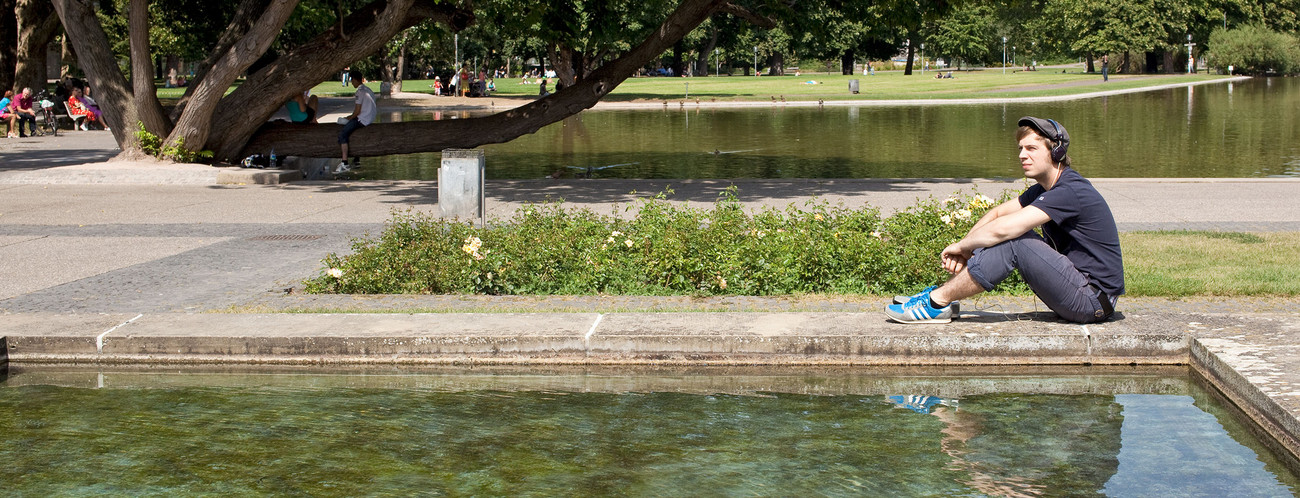 A young man sitting in a park listening to some tunes.