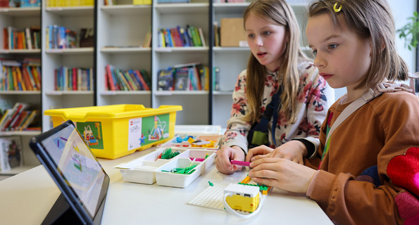Zwei Mädchen bauen einen von einem Tablet aus steuerbaren Roboter in der Grundschule.