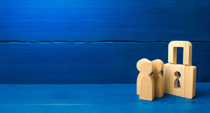 Ein hölzernes Vorhängeschloss und drei hölzerne Figuren stehen vor einer blauen Wand.