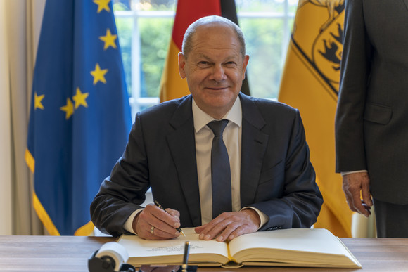 Bundeskanzler Olaf Scholz sitzt im Runden Saal der Villa Reitzenstein in Stuttgart und trägt sich in das Gästebuch des Landes ein.