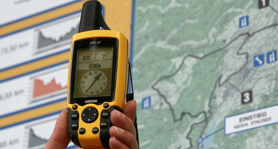 Jemand hält einen GPS-Empfänger vor einer Karte in der Hand (Bild: © dpa).