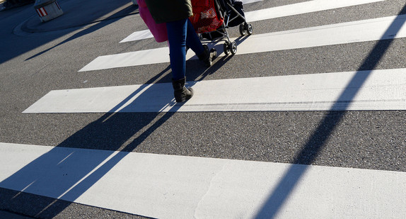 Eine Mutter geht mit einem Kinderwagen über einen Zebrastreifen.