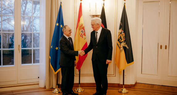 Ministerpräsident Winfried Kretschmann (rechts) und der spanische Botschafter Pascual Ignacio Navarro Rios (links) stehen vor Fahnen und geben sich die Hand.