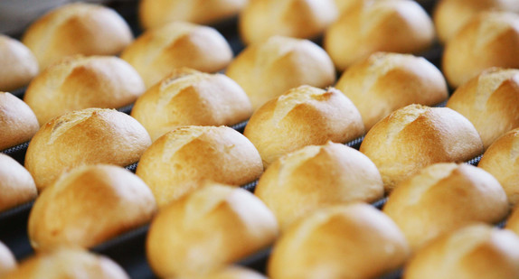 Symbolbild: Brötchen auf dem Fließband kommen aus dem Ofen. (Bild: Achim Scheidemann / dpa)