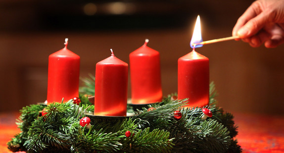 Eine Frau entzündet an einem selbst gebundenen Adventskranz eine Kerze. (Foto: © dpa)